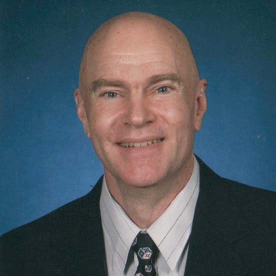 A smiling white bald man wearing a black suit coat over a white pin striped shirt and tie.